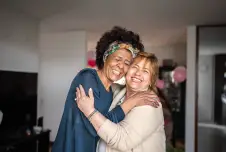 Two friends hugging each other and smiling, inside a house
