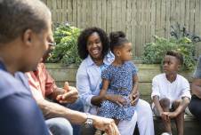 Black adults and kids sitting in a backyard and talking