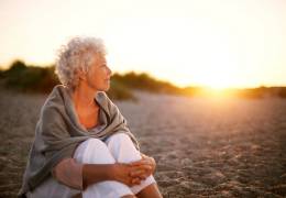 Older woman sitting on the beach at sunset